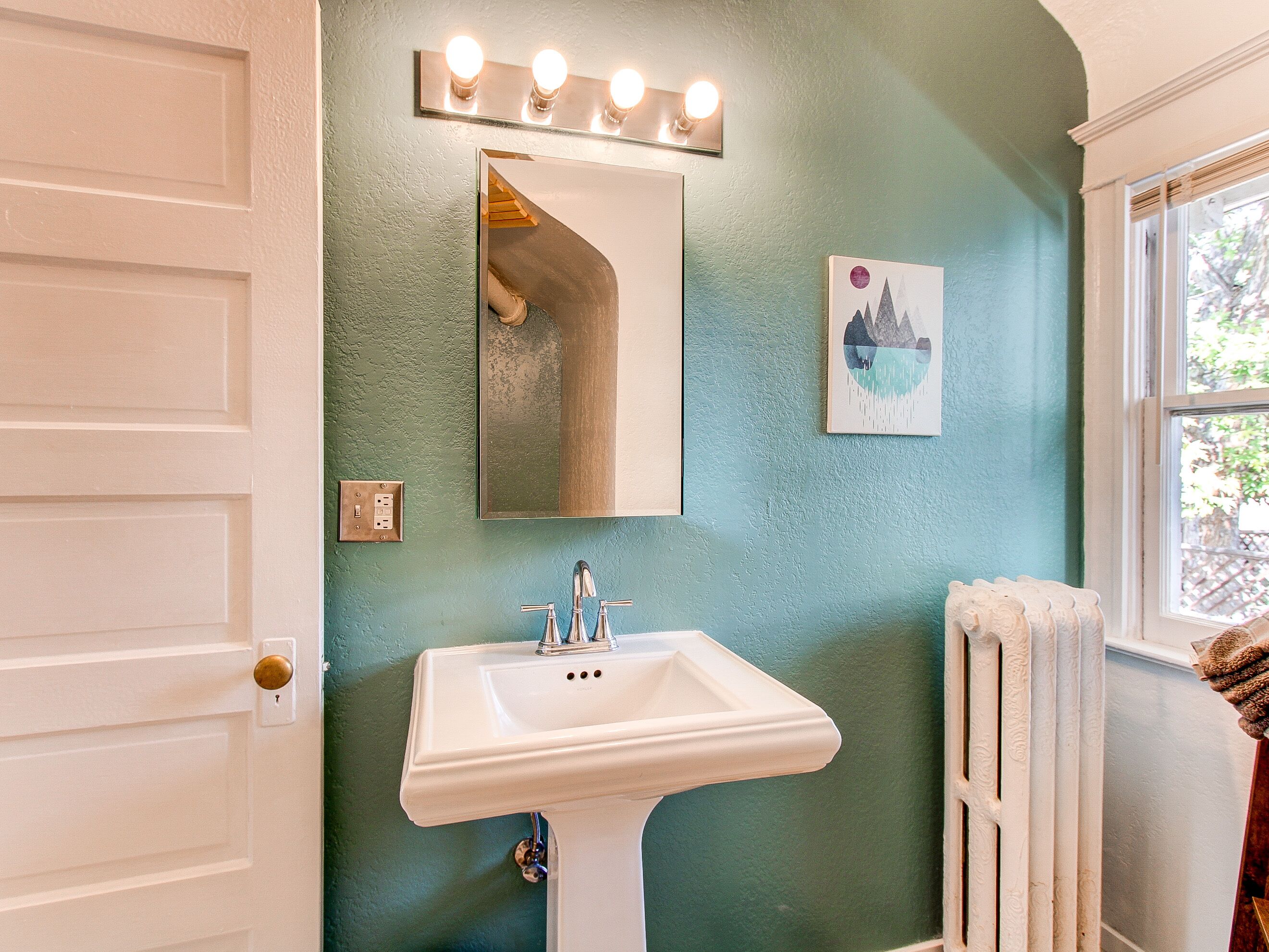 A bathroom with a white sink, a mirror with lights, and a radiator.