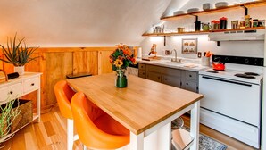 Une cuisine compacte avec des meubles en bois, un poêle blanc et une table à manger en bois, assortie de chaises orange.