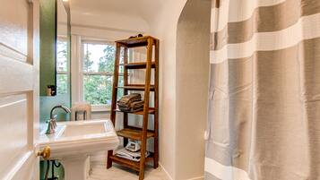 A bathroom with a wooden shelf holding towels, a sink, and a mirror.