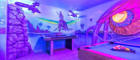 Une pièce dotée d’une table de billard, d’une fresque murale sur un thème fantastique et d’une fenêtre circulaire originale.