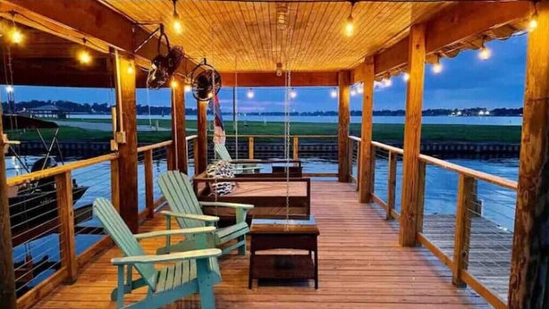 Una terraza de madera con sillas y mesas, con vista a un cuerpo de agua.
