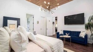Un dormitorio moderno con una cama grande, un sofá azul, un televisor y una lámpara de techo original.