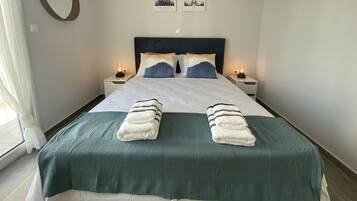 A neatly made bed with a green bedspread and two towels, two bedside tables with lamps, a wall-mounted air conditioner, and two framed pictures of the Eiffel Tower.