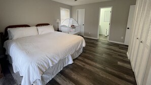 Een slaapkamer met een groot bed, een plafondventilator, een wieg en een deur naar een andere kamer.