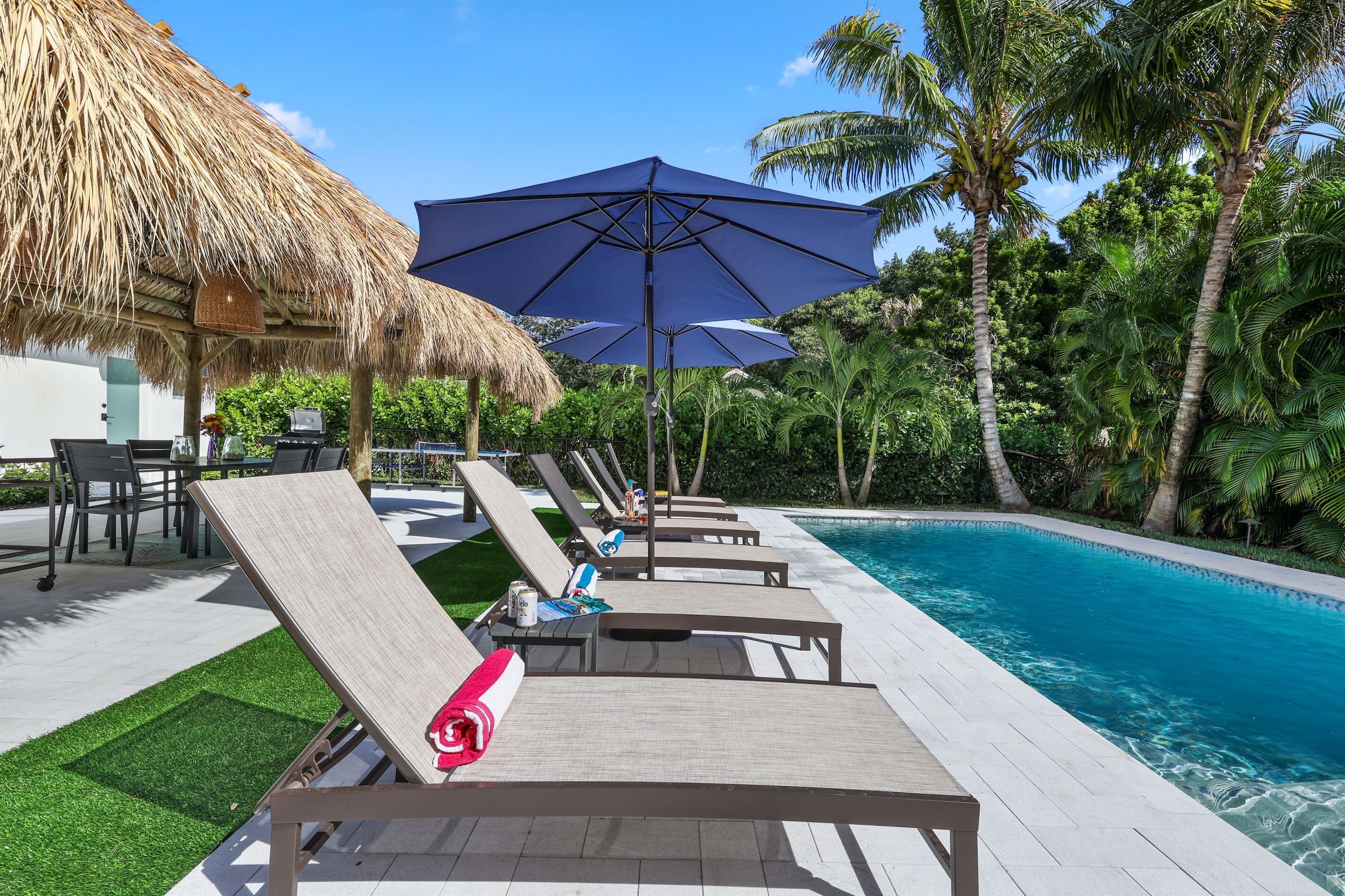 Un espace aménagé au bord de la piscine, avec des chaises longues, un toit de chaume et un grand parasol.