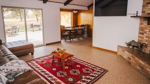 Ein Wohnzimmer mit braunem Ledersofa, einem roten Teppich mit Muster und einem Kamin aus Backsteinen.