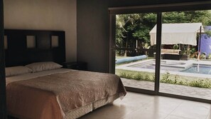 Un dormitori amb un llit gran, una tauleta de nit i vista a una piscina exterior a través d'una porta corredissa de vidre.