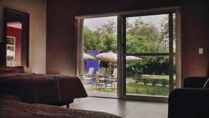Una stanza con un letto, una sedia e un'ampia porta-finestra scorrevole che dà su un'area esterna con piscina e ombrelloni.