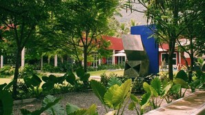 Un jardí amb plantes verdes grans i un edifici amb teulada vermella.