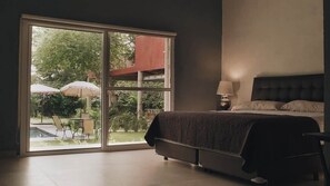 Un dormitori amb un llit, una taula de nit, una làmpada i una porta corredissa de vidre que dona a una zona exterior amb caires i ombrelles.