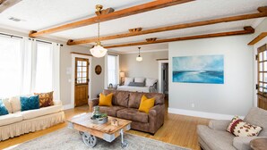 Ein Wohnzimmer mit Holzboden, ein braunes Sofa mit gelben Kissen, ein beiges Sofa mit blauen Kissen und ein Couchtisch aus Holz.