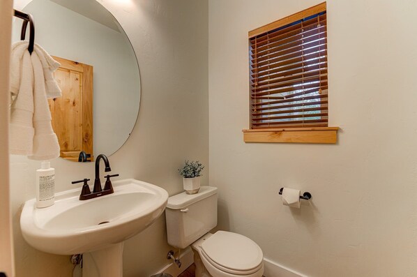 A bathroom with a white sink, a toilet, a mirror, and a window with blinds.