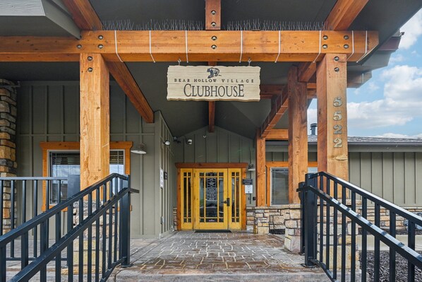 Una entrada de madera con un letrero que dice 'BEAR HOLLOW VILLAGE CLUBHOUSE' y una escalera de piedra que sube hasta la puerta.