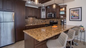 Eine Küche mit dunklen Holzschränken, Granit Arbeitsplatten, Edelstahlgeräten und Pendelleuchten.