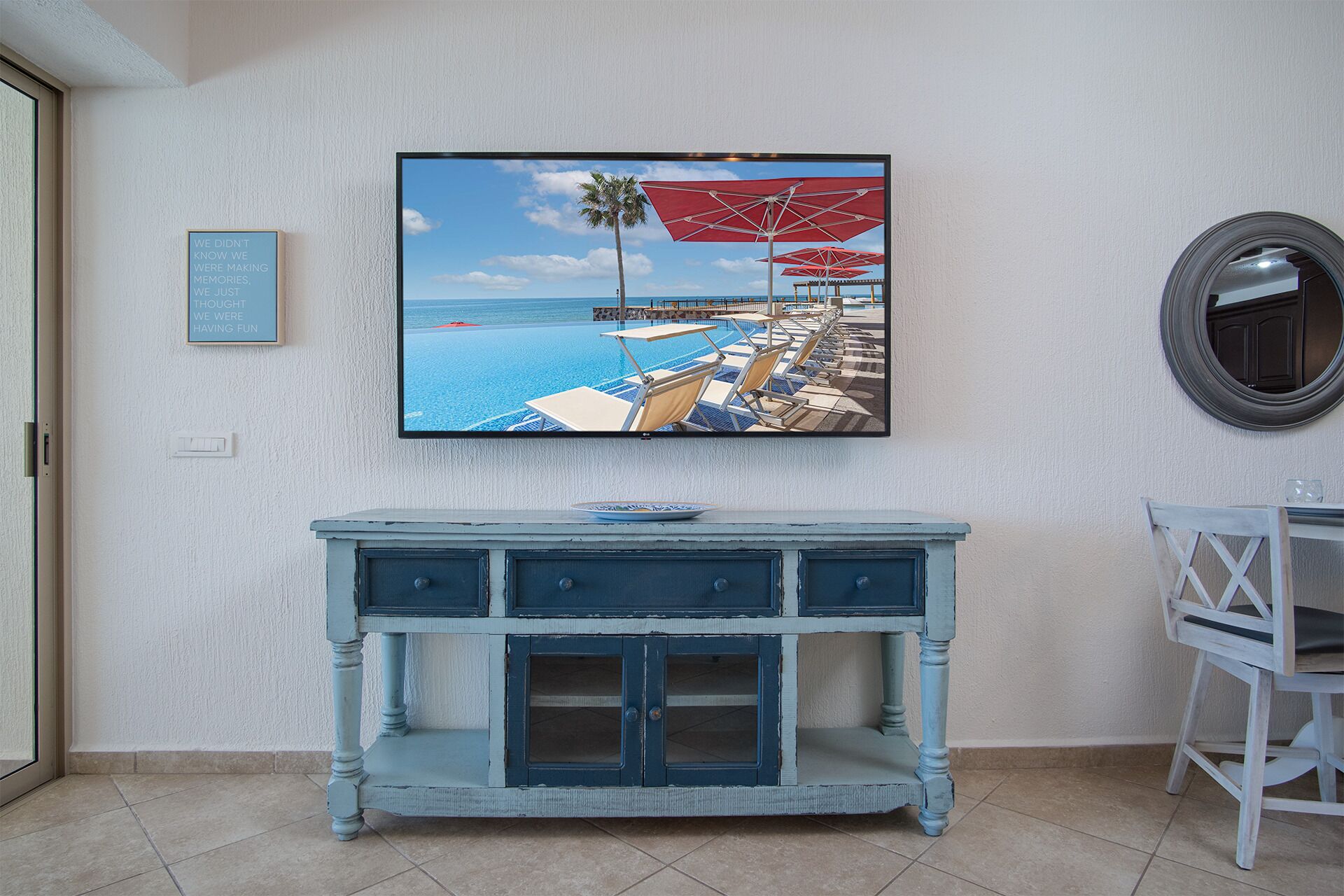 A room with a television mounted on the wall displaying a beach scene.