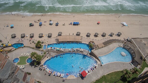 Eine Vogelperspektive eines Strandresorts mit mehreren Schwimmbecken, Strandstühlen und Liegen.