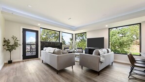 Ein modernes Wohnzimmer mit zwei Sofas, einem Flachbildfernseher und großen Fenstern mit Blick ins Freie.