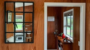 Un intérieur en bois avec un mur miroir, un four à micro-ondes, un petit tabouret et une fenêtre donnant sur un paysage verdoyant.