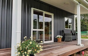 Et moderne hus med mørk facade, store skydedøre i glas, en træterrasse og udendørs møbler.