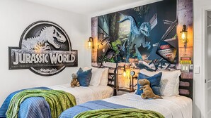 A bedroom with two beds, a 'Jurassic World' themed mural, dinosaur plush toys, and a 'Danger' sign.