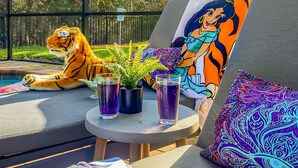 A poolside lounge with a tiger plush toy, two potted plants, and two glasses of purple drink.