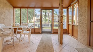 Uma área de varanda coberta com mesa, cadeiras, janelas amplas e vista para o exterior.