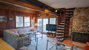 A cozy living room with a sofa, TV, and fireplace. A staircase leads to a balcony. - Mountain-View Condo with fireplace, pool, hot tub, and ski access. (Durango)