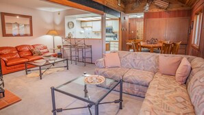 A cozy living room with a red leather sofa, a patterned sofa, and a glass coffee table. There is a kitchen area visible in the background. - Mountain-View Condo with fireplace, pool, hot tub, and ski access. (Durango)