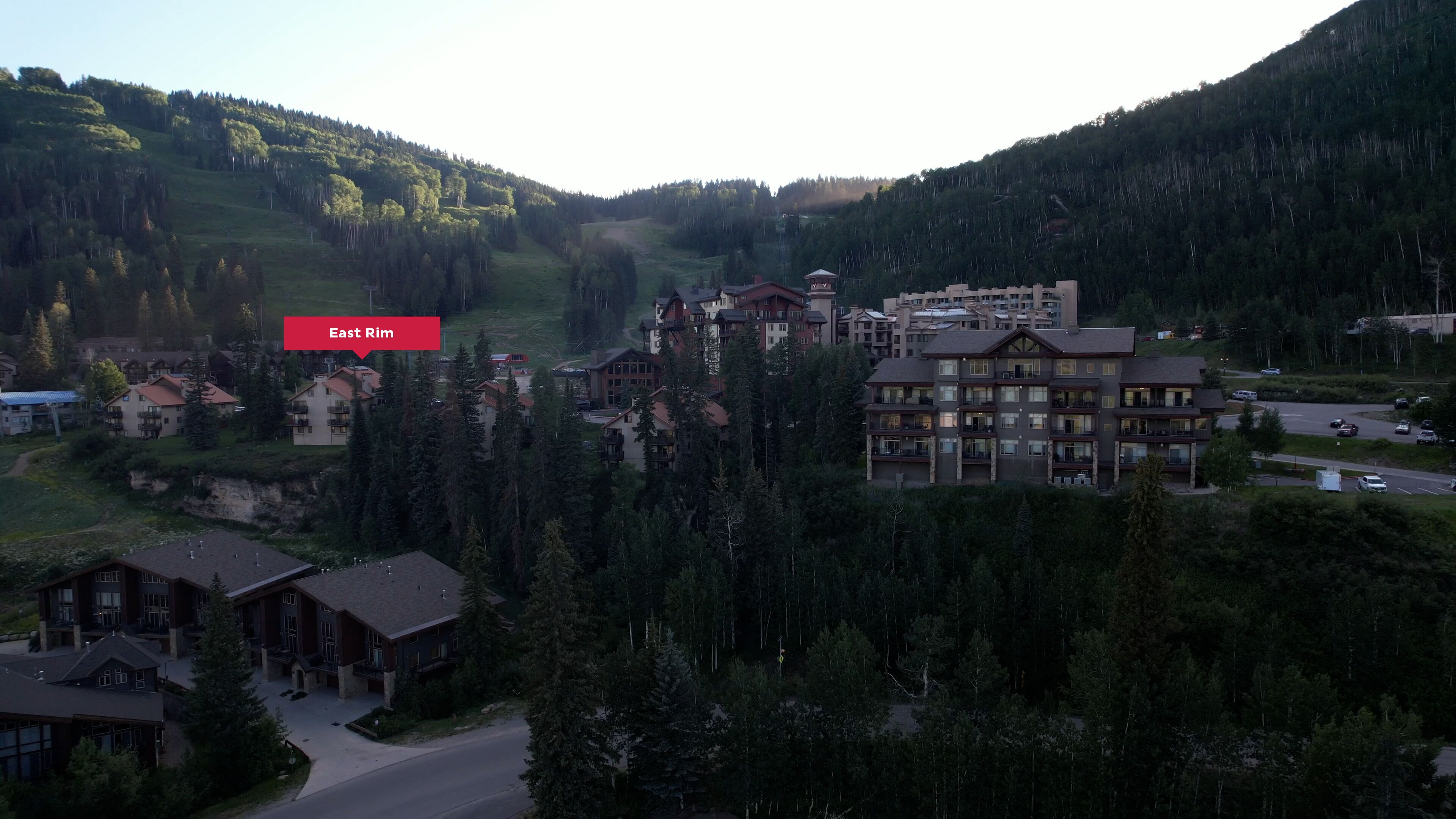 A resort with multiple buildings, including a large lodge with a ski lift, surrounded by forested hills.