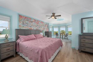A bedroom with a bed, a desk, a chair, a ceiling fan, and a large window. - Absolute Searenity- Oceanfront, Pet-Friendly, Private Pool and Hot Tub (Nags Head)