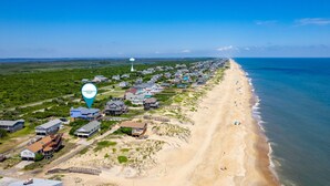 A coastal town with beachfront properties, a lighthouse, and a beach with people. - Absolute Searenity- Oceanfront, Pet-Friendly, Private Pool and Hot Tub (Nags Head)