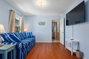 A living room with a sofa, a TV, and a hallway leading to another room. - Absolute Searenity- Oceanfront, Pet-Friendly, Private Pool and Hot Tub (Nags Head)