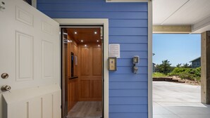 A hotel entrance with a blue exterior wall, a white door, and a wooden elevator. - Absolute Searenity- Oceanfront, Pet-Friendly, Private Pool and Hot Tub (Nags Head)