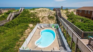 A swimming pool with a wooden deck, surrounded by sand dunes and greenery, with a view of the ocean. - Absolute Searenity- Oceanfront, Pet-Friendly, Private Pool and Hot Tub (Nags Head)