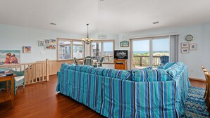 A spacious room with a large bed, a ceiling fan, a dining area, and a view of the ocean. - Absolute Searenity- Oceanfront, Pet-Friendly, Private Pool and Hot Tub (Nags Head)