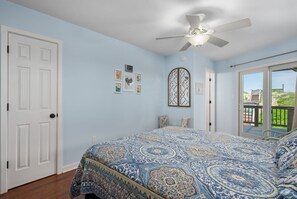 A bedroom with a large bed, a ceiling fan, and a view of the outdoors through a sliding glass door. - Absolute Searenity- Oceanfront, Pet-Friendly, Private Pool and Hot Tub (Nags Head)