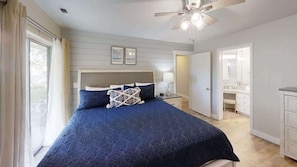 Une chambre à coucher avec un lit, des tables de chevet, un ventilateur de plafond et une fenêtre avec des rideaux.