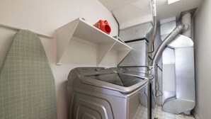 A laundry room with a washing machine, a drying rack, and a shelf with a red mug.