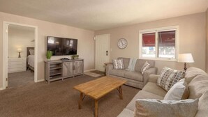 A living room with a flat-screen TV, a wooden coffee table, a sofa, and a window with a view. - Las Palmas Resort #1616 | All-Inclusive Amenities (Saint George)