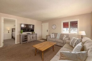 A living room with a flat-screen TV, a wooden coffee table, a sofa, and a window with a view. - Las Palmas Resort #1616 | All-Inclusive Amenities (Saint George)
