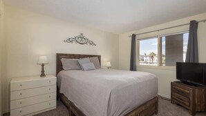 A bedroom with a bed, bedside tables, a television, and a window with curtains. - Las Palmas Resort #1616 | All-Inclusive Amenities (Saint George)