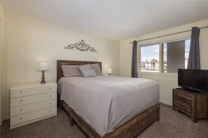 A bedroom with a bed, bedside tables, a television, and a window with curtains. - Las Palmas Resort #1616 | All-Inclusive Amenities (Saint George)