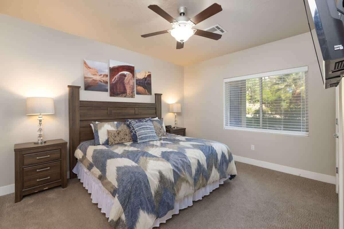 A bedroom with a bed, two bedside tables, a ceiling fan, and a window with blinds.