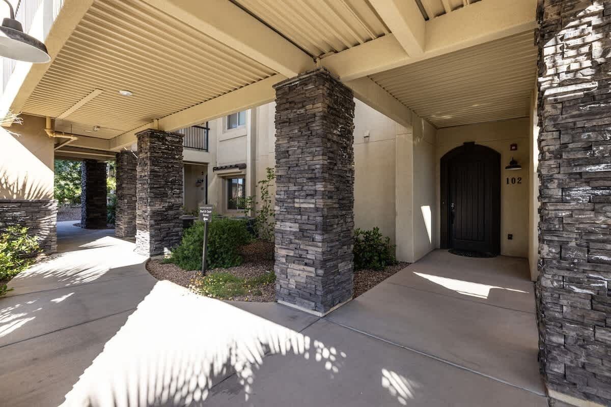 A covered entrance with stone pillars, a concrete driveway, and a dark door marked with the number 102.