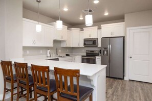 A kitchen with white cabinets, stainless steel appliances, and a central island with bar stools.