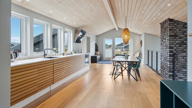 A modern kitchen with a wooden ceiling, large windows, and a dining area with a table and chairs.