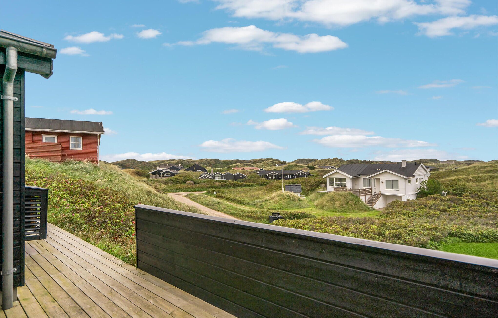 A coastal landscape with a wooden deck overlooking a series of houses on a grassy hill.