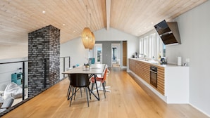 A modern kitchen with a wooden ceiling, a stone fireplace, and a dining area with a table and chairs.