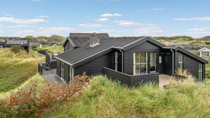 A modern black house with a sloped roof, large windows, and a deck.