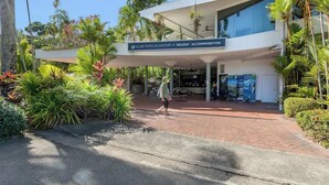Um edifício moderno com uma placa para Club Tropical Resort, apresentando uma entrada coberta e paisagismo tropical exuberante.